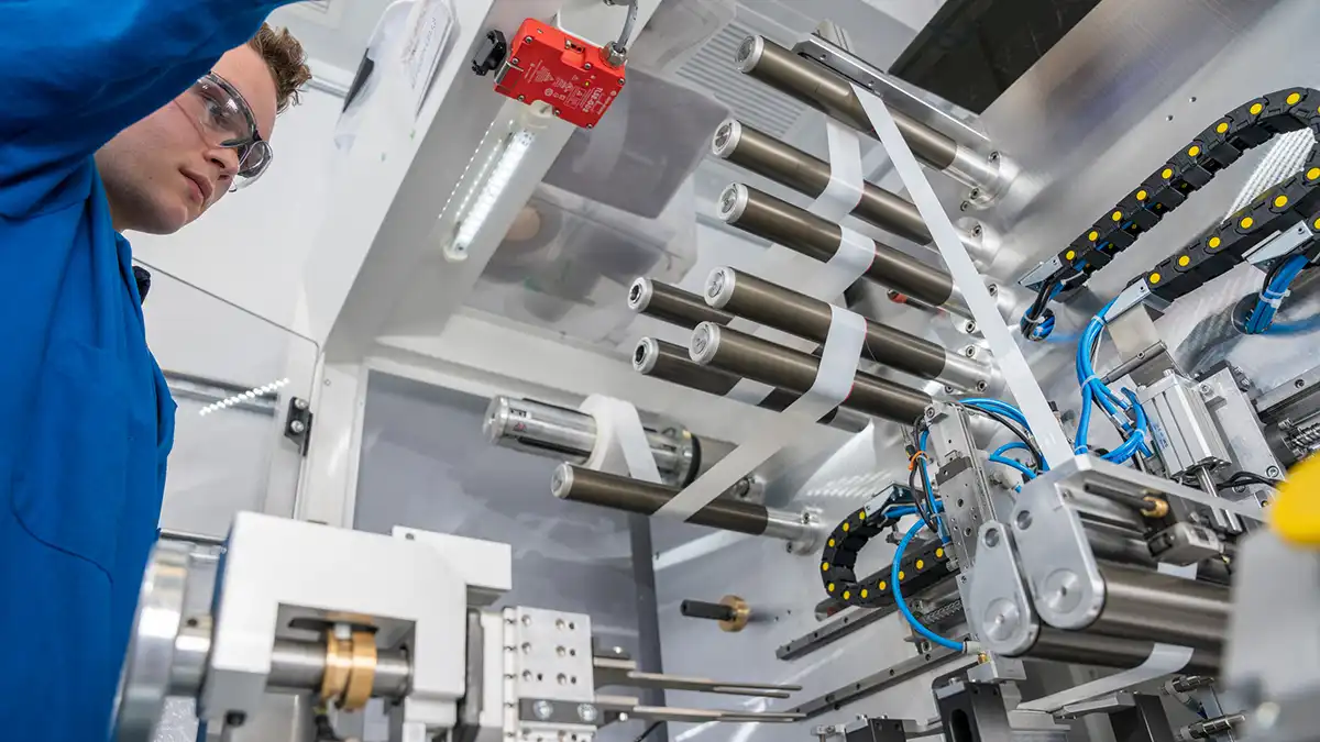 Technician in blue lab coat inspects cylindrical rollers and machinery used for battery film processing.