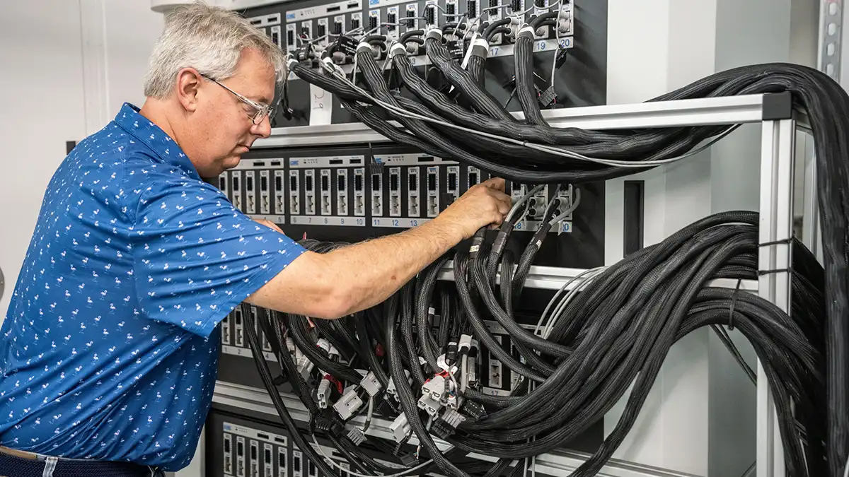 Engineer works with a panel of electrical connectors and cables in a battery testing setup.