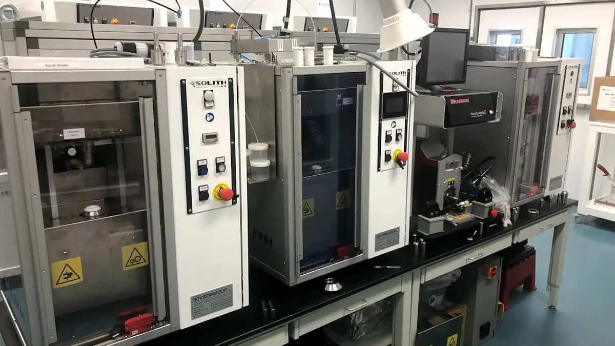 Industrial equipment used for cylindrical cell battery assembly and finishing in a lab setting.