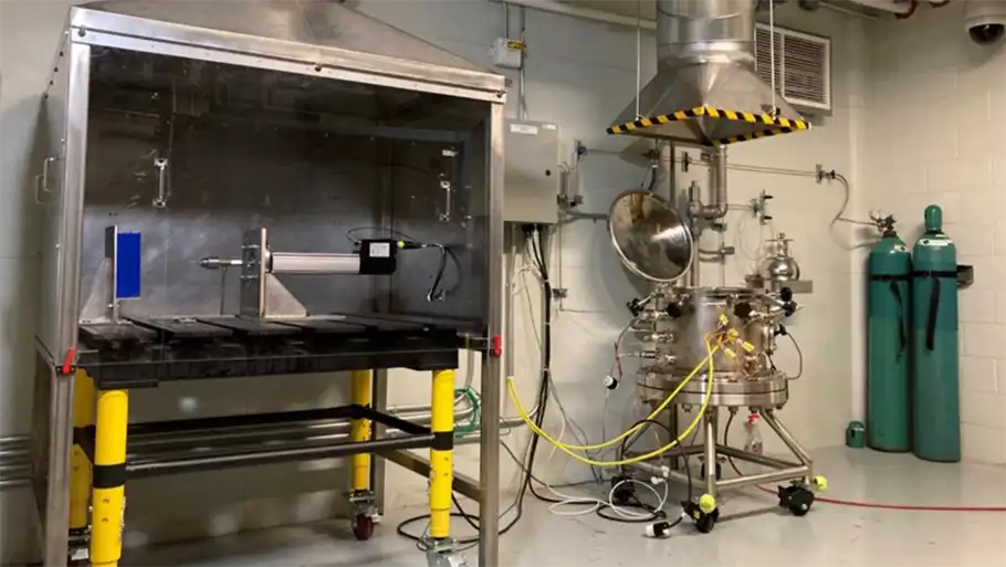 Lab equipment including an enclosed space with a glass panel for observing battery fire tests.