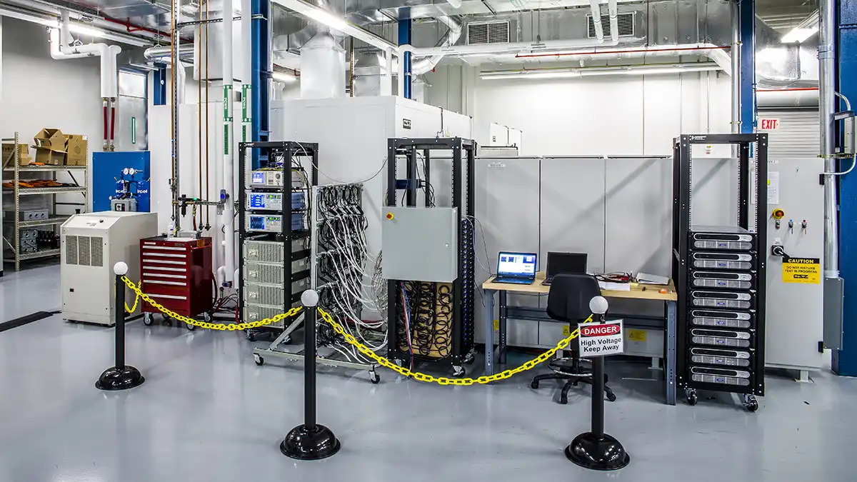 High-voltage battery performance testing area with computers and monitoring equipment behind safety barriers.