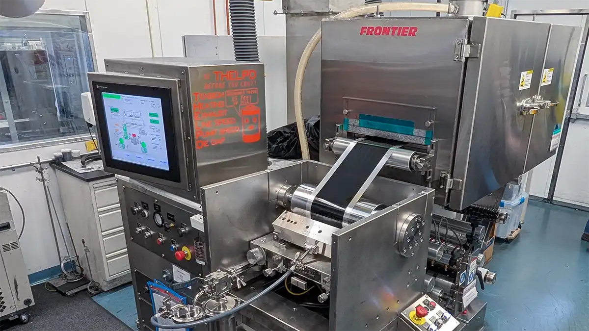 Large roll-to-roll coating machine applying electrode material onto a battery substrate.