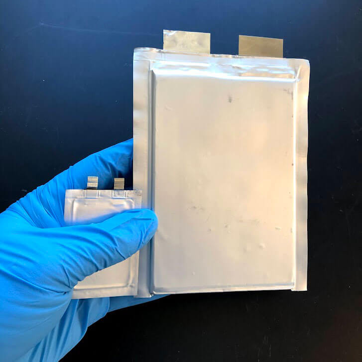 A gloved hand holding a small pouch cell and a larger pouch cell.