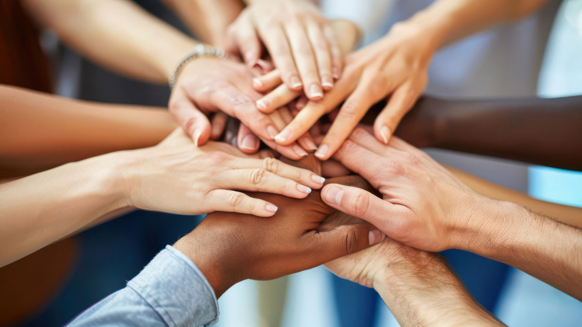 A circle of people reach their hands into the center to show comradery.