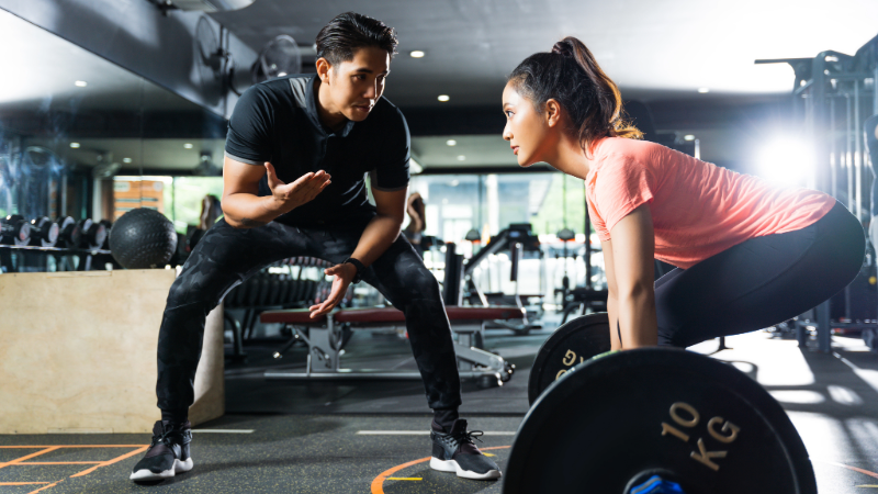Personal trainer encouraging client to deadlift a barbell