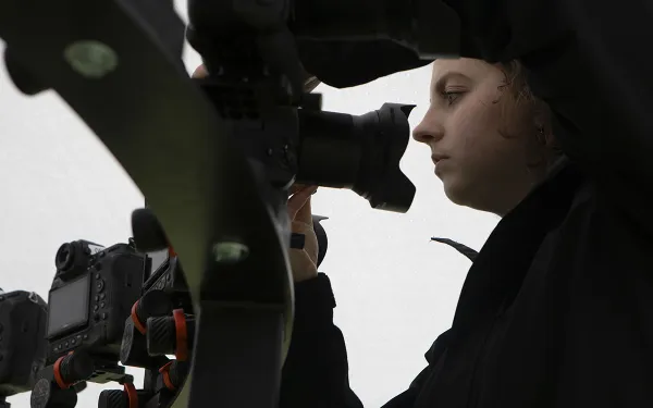 A student looks into a camera lens.