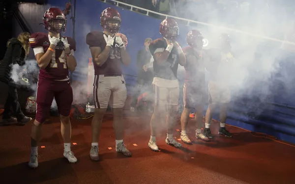 Football players stand as a smoke machine operates behind them.