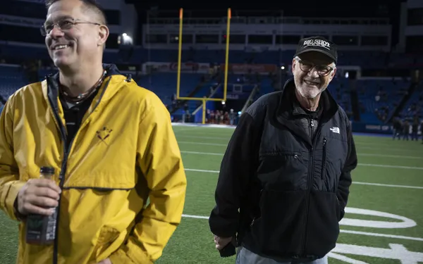 Eric Kunsman and Michael Peres smile on the Highmark Stadium field.