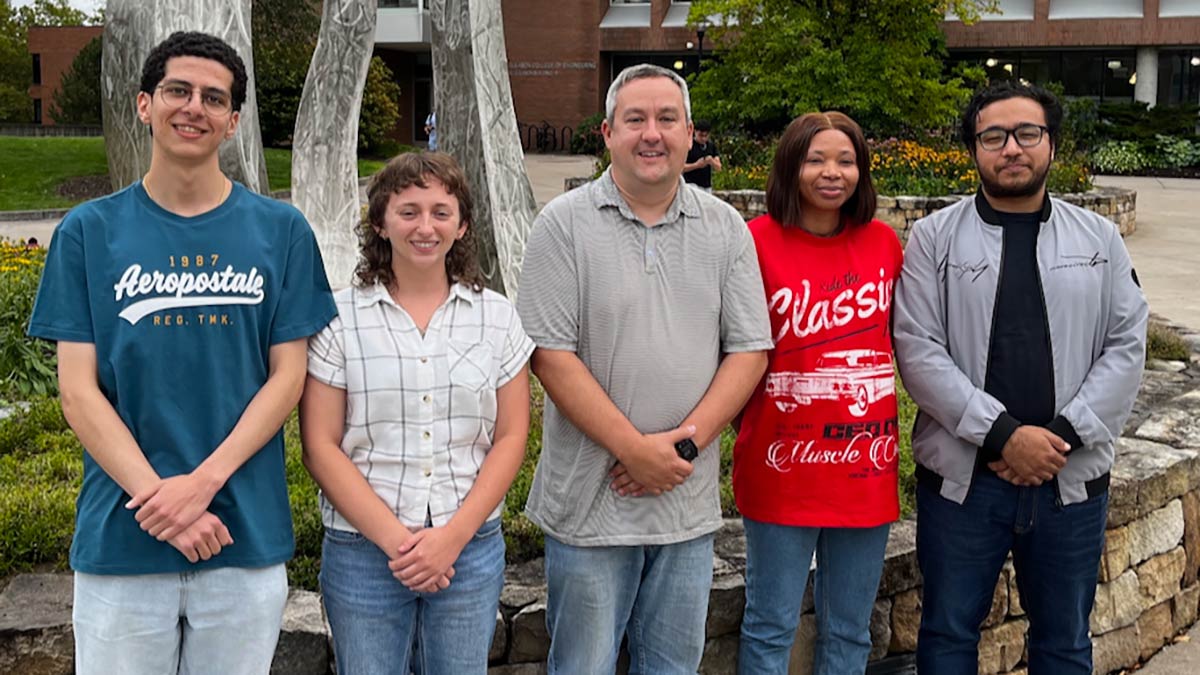 a professor and four students pose outdoors for a photo.