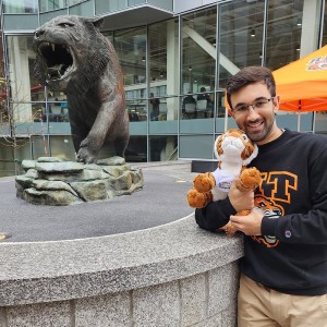 Male student smiling with stuffed tiger toy and a tiger sculpture in the background