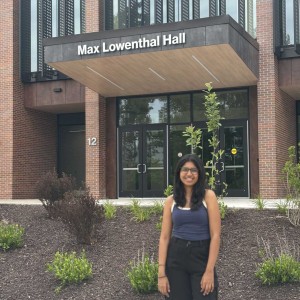 Student standing in front of campus residence hall smiling