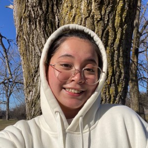 Student in a hooded sweatshirt smiling in front of a tree