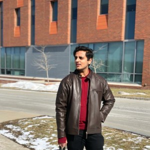 Moin Stands on a city street with one hand in his pocket. 