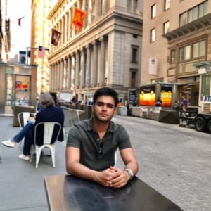  Rutvik sits at a cafe table on the side of a city street.