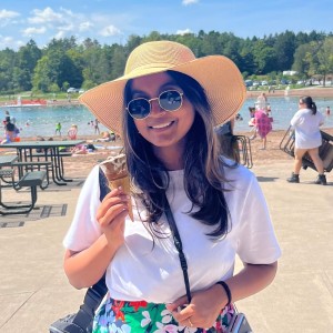 A girl in a sun hat and sunglasses, holding an ice cream cone at the beach