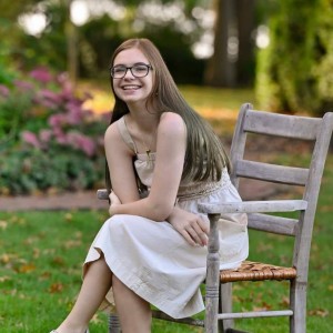 Student sitting in wooden chair outside in a long dress