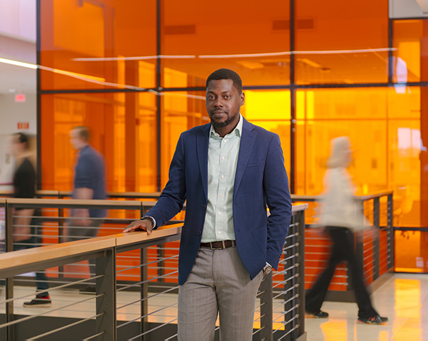 Man in sports coat standing with his hand on a railing in front of an orange glass room