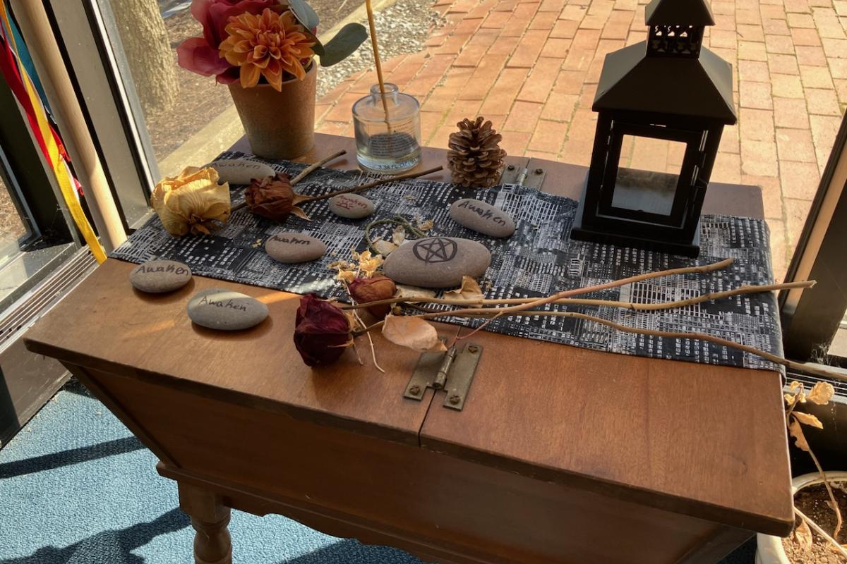 Pagan altar with symbolic stones, candles, flowers, natural materials, and a lantern arranged on a wooden table.