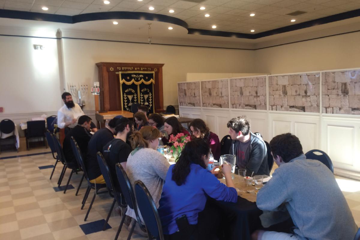 Students and community members sit together at a long dining table in a community gathering space.