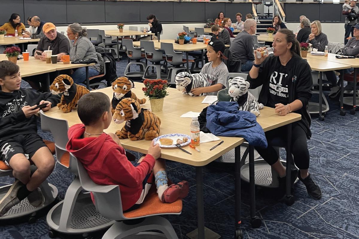 Participants sit around tables with stuffed tiger mascots during a community event in a large gathering space.