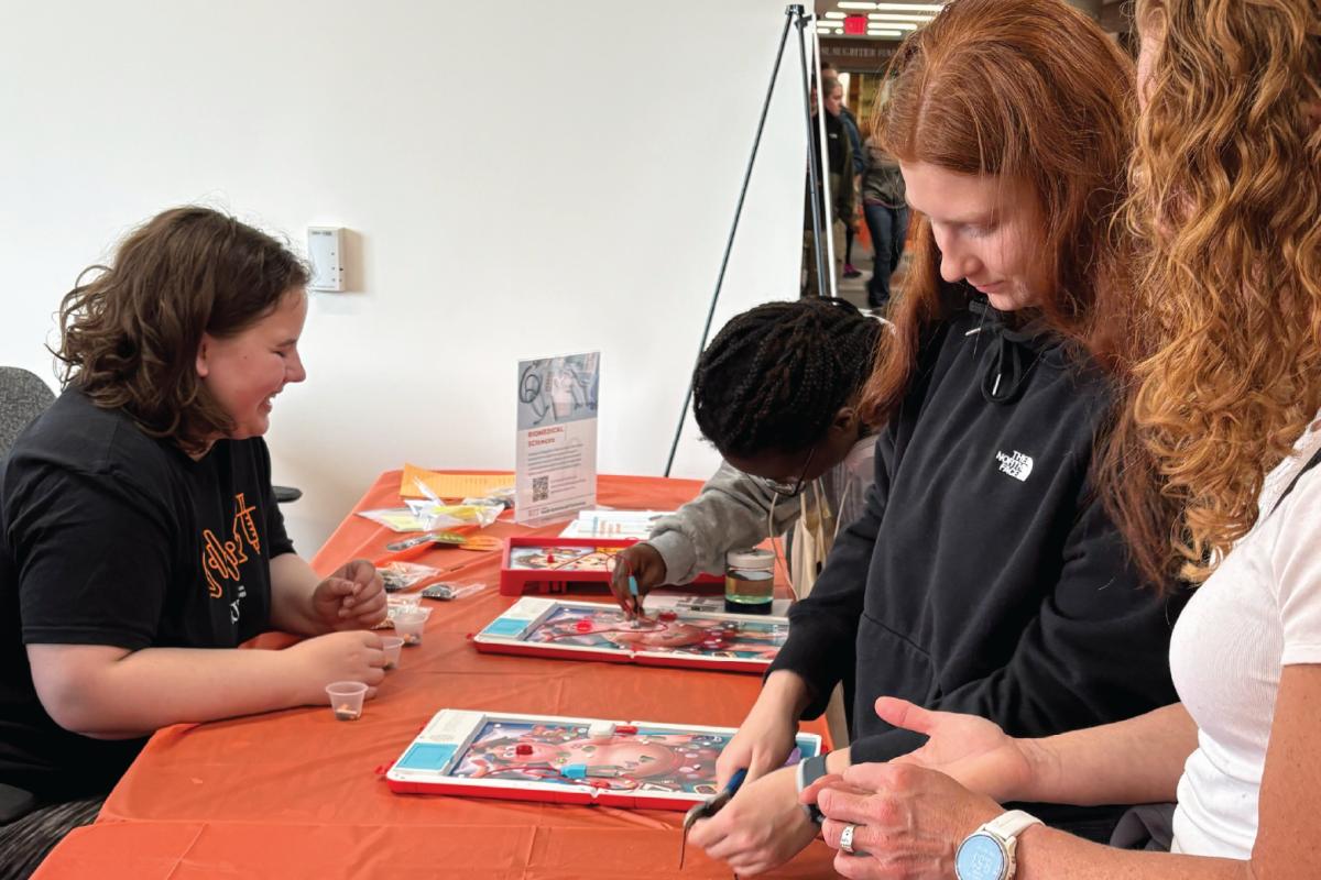 Group of four standing around a table with two Operation board games actively participating in an educational activity.