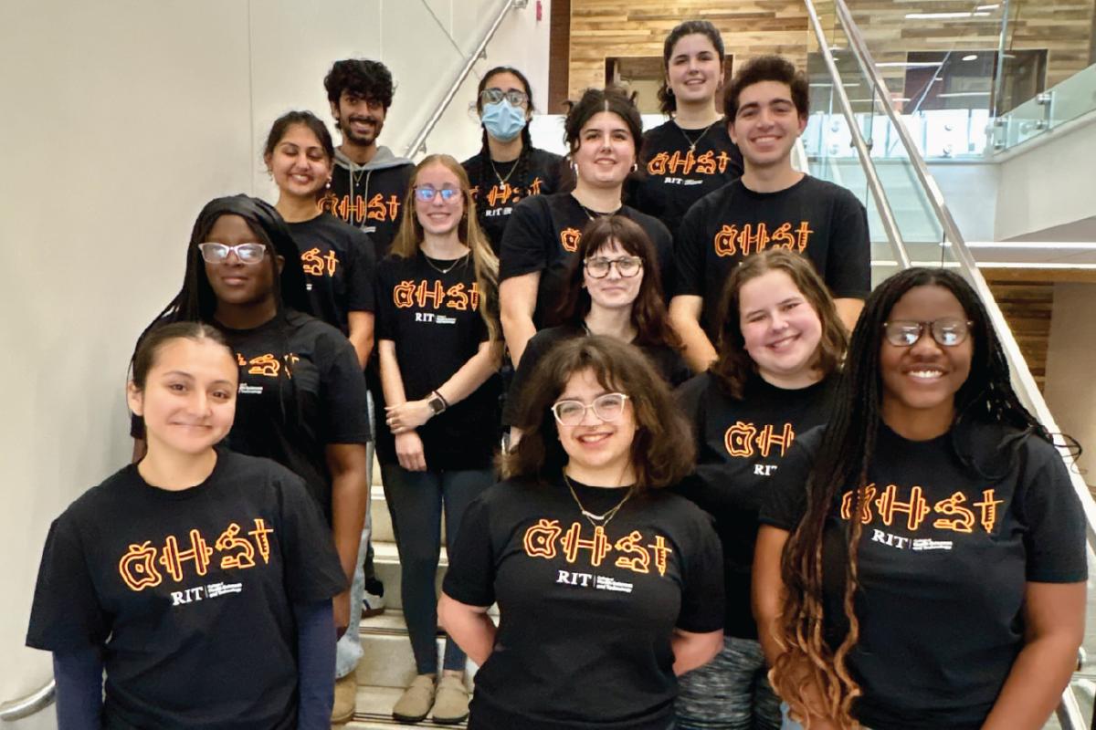 Group of CHST students wearing black College of Health Sciences and Technology t-shirts featuring the limited-edition Brick City Weekend design. The students are gathered on a staircase inside an RIT building and smiling at the camera.