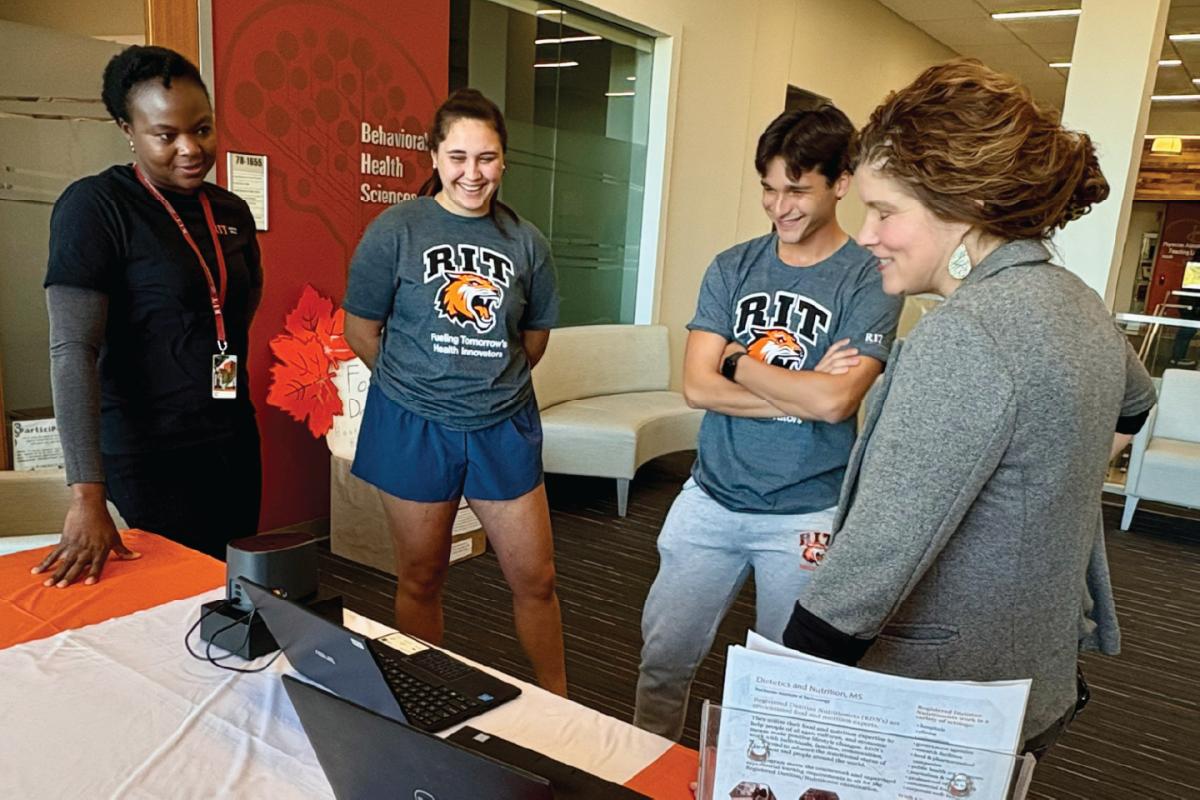 Four people gathered around a table with a laptop and Veggie Meter device, two wearing gray RIT shirts.