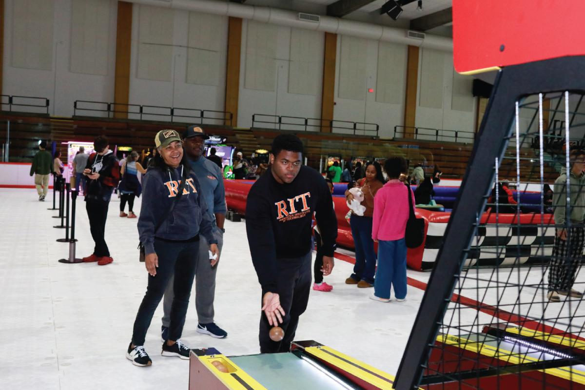 Participants play an arcade-style ball-toss game on an indoor rink floor while families and visitors enjoy activities throughout the Family Fun Zone.