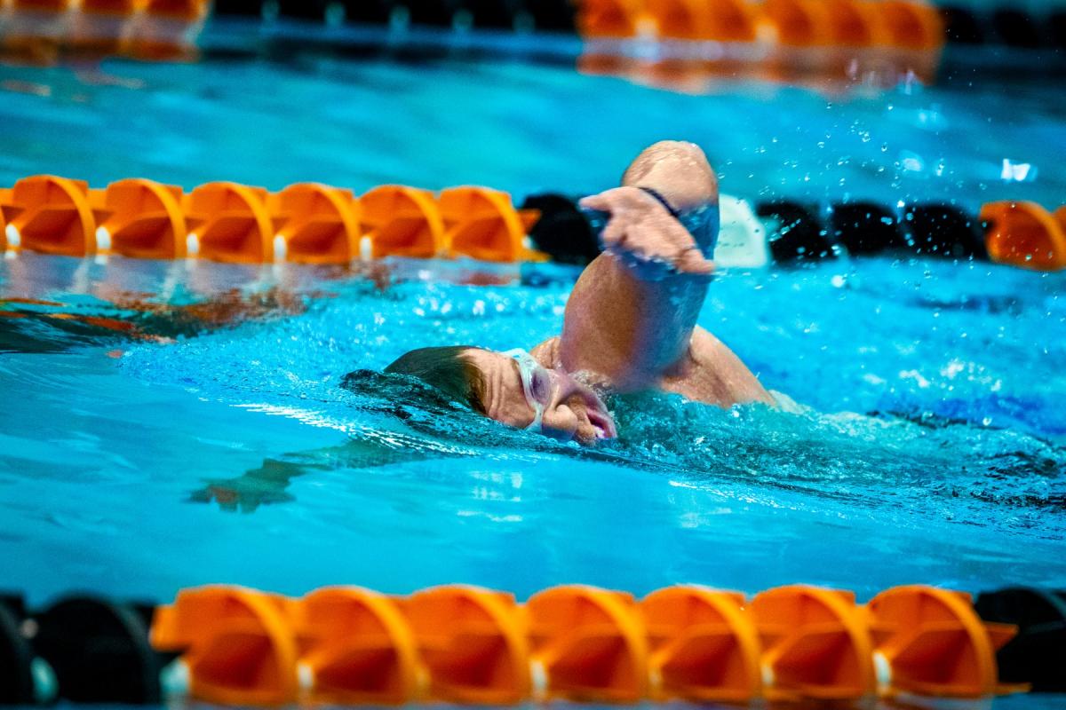 Swimmer wearing goggles performs the freestyle stroke in a lane of an indoor swimming pool.