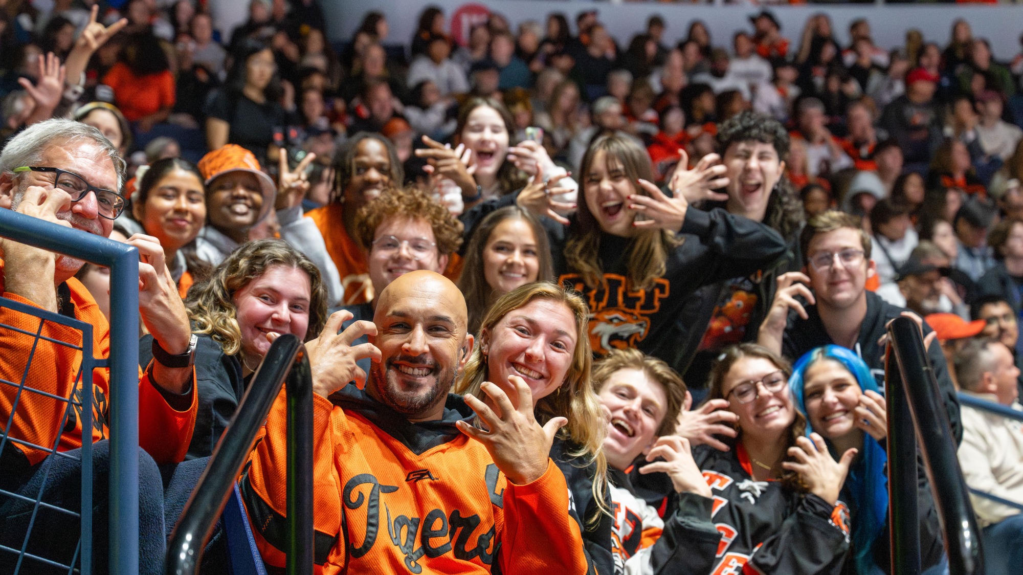 Group of RIT fans wearing team apparel gathers in the arena stands during a hockey game.
