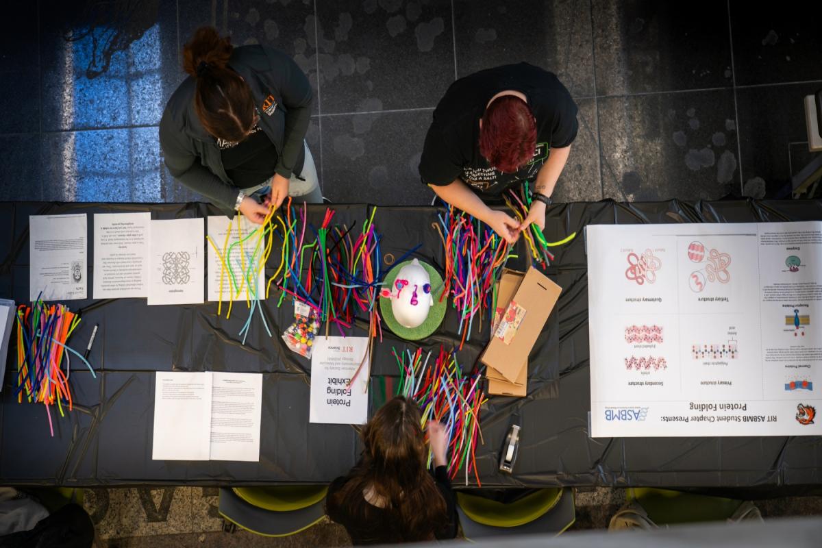 Overhead view of participants using colorful pipe cleaners to build protein structure models at a science fair exhibit.