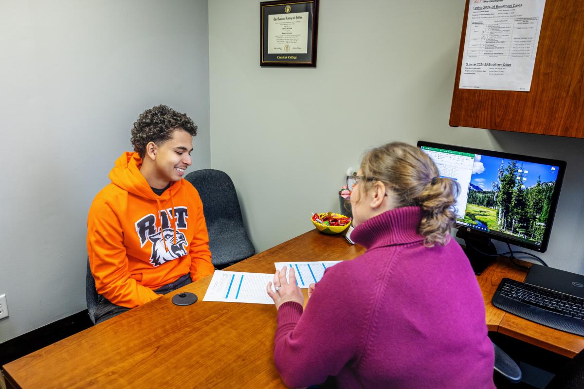 Student and staff member sit across a desk reviewing documents during an advising appointment in a campus office.