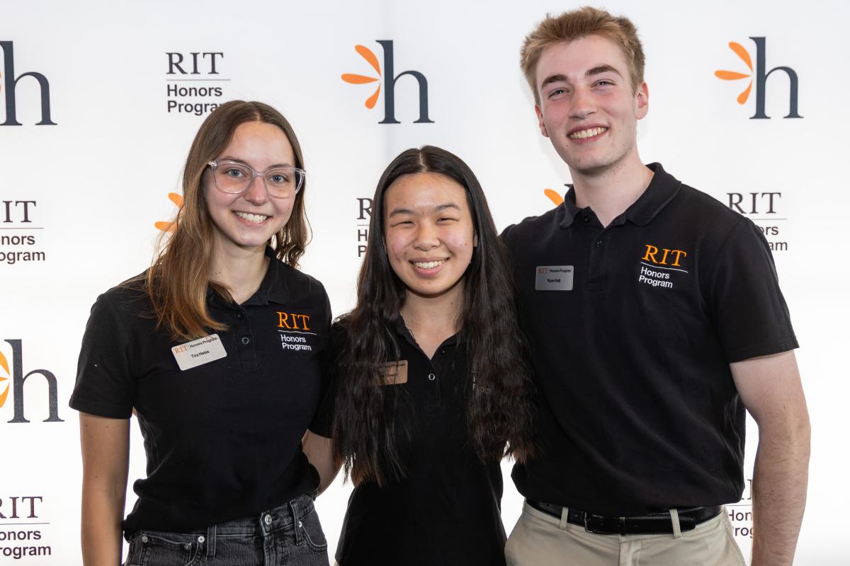 Three RIT Honors Program students smiling and posing together in front of an RIT Honors Program backdrop.