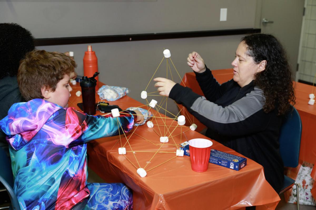 Two people building a tower using marshmallows and spaghetti