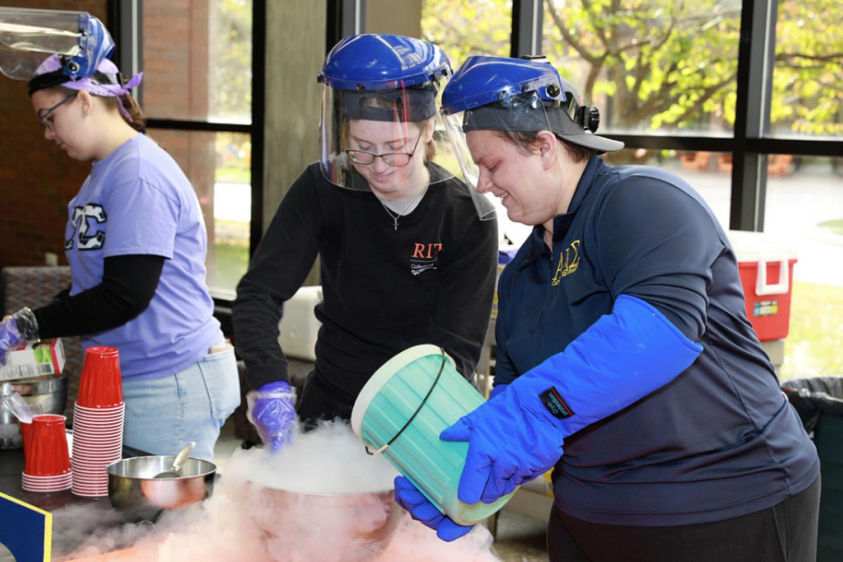 Two people making ice cream with a bucket of nitrogen and stirring