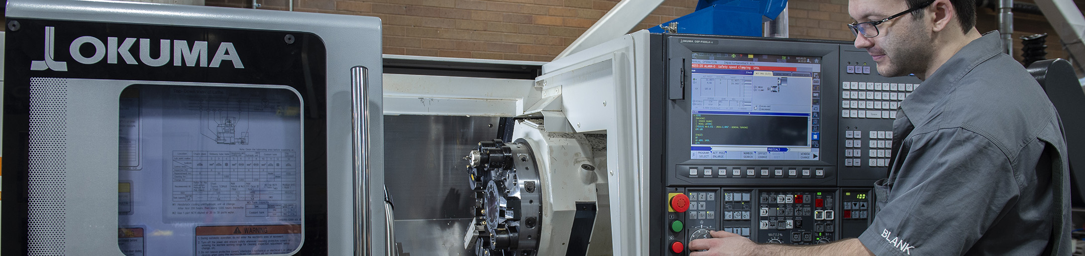 Person operating an OKUMA GENOS L2000-e CNC lathe in an industrial workshop
