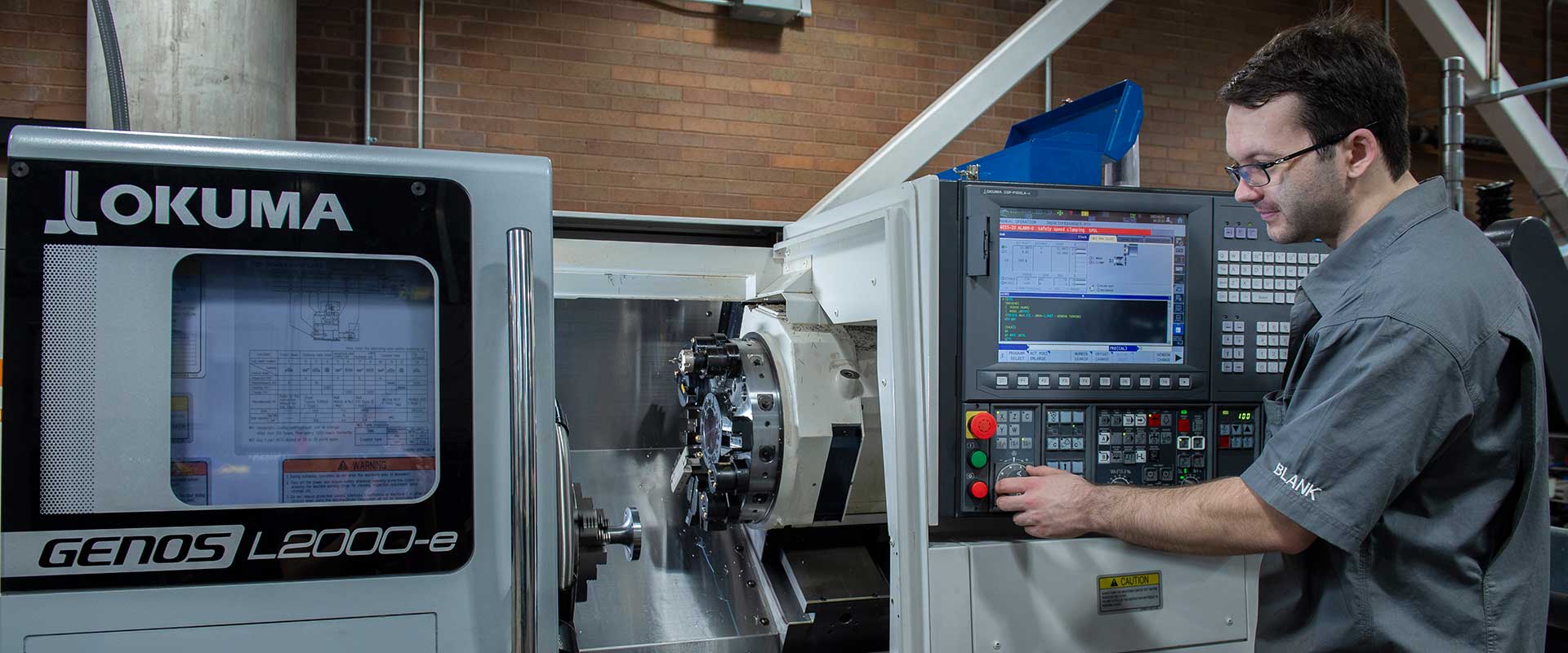 Person operating an OKUMA GENOS L2000-e CNC lathe in an industrial workshop.