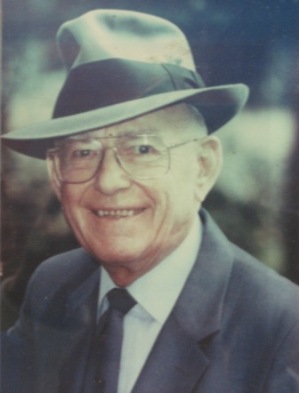 Earl W. Brinkman head shot wearing a fedora, suite, and tie