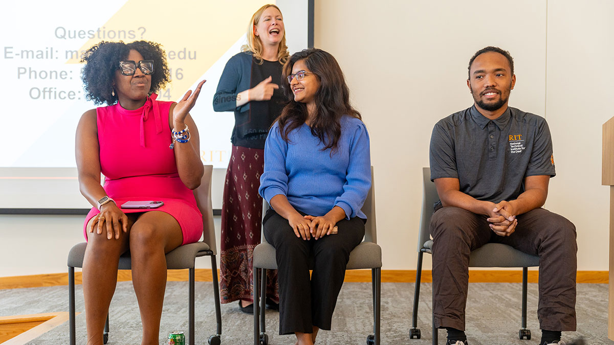 A group of professionals sitting on chairs in a panel discussion with a sign language interpreter in the background.