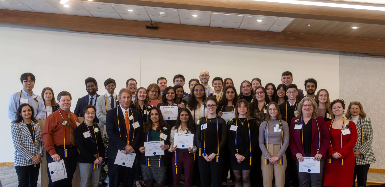 A group photo of students and faculty on stage, holding certificates during an award ceremony.