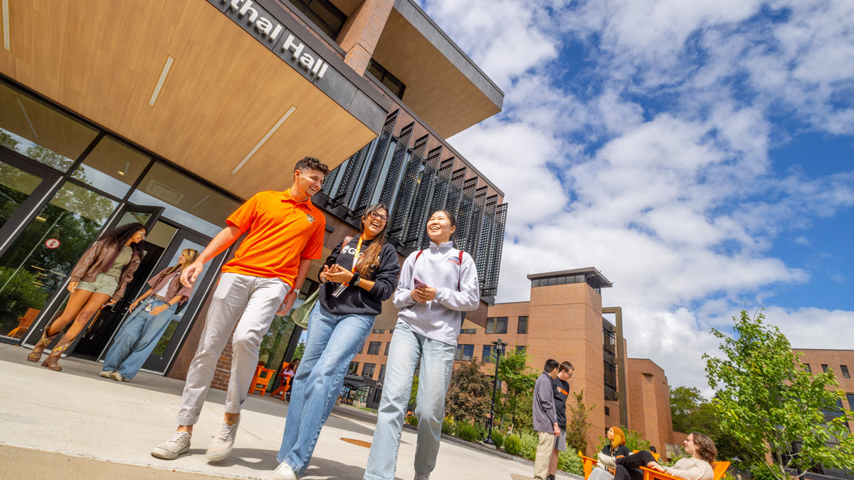 Students standing outside a campus building, chatting and enjoying the sunny weather.