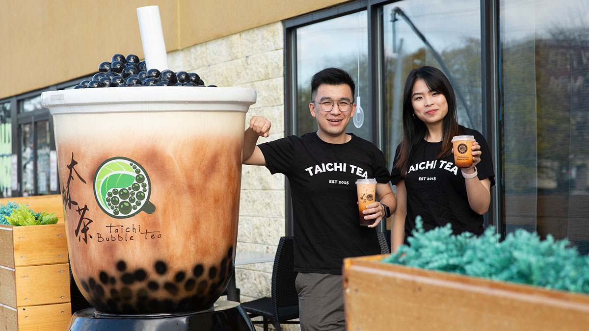 Two people posing next to a large take-out cup statue at the Taichi Tea restaurant.