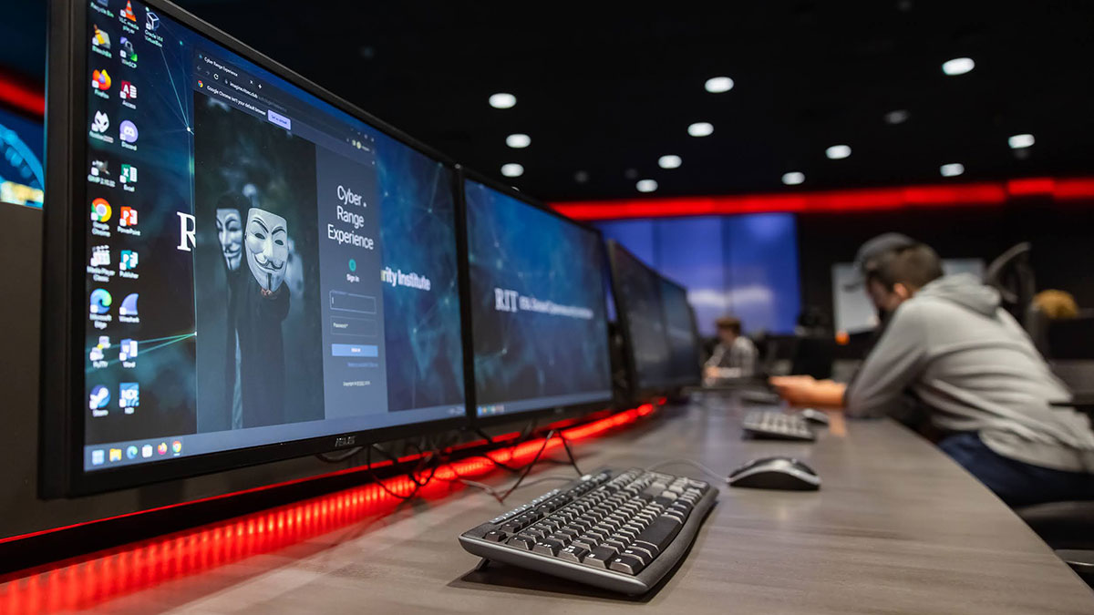 A row of computer monitors displaying a cybersecurity simulation in a lab environment.