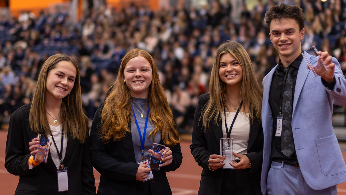 A group of four students dressed in professional attire smiling and holding awards at an event.