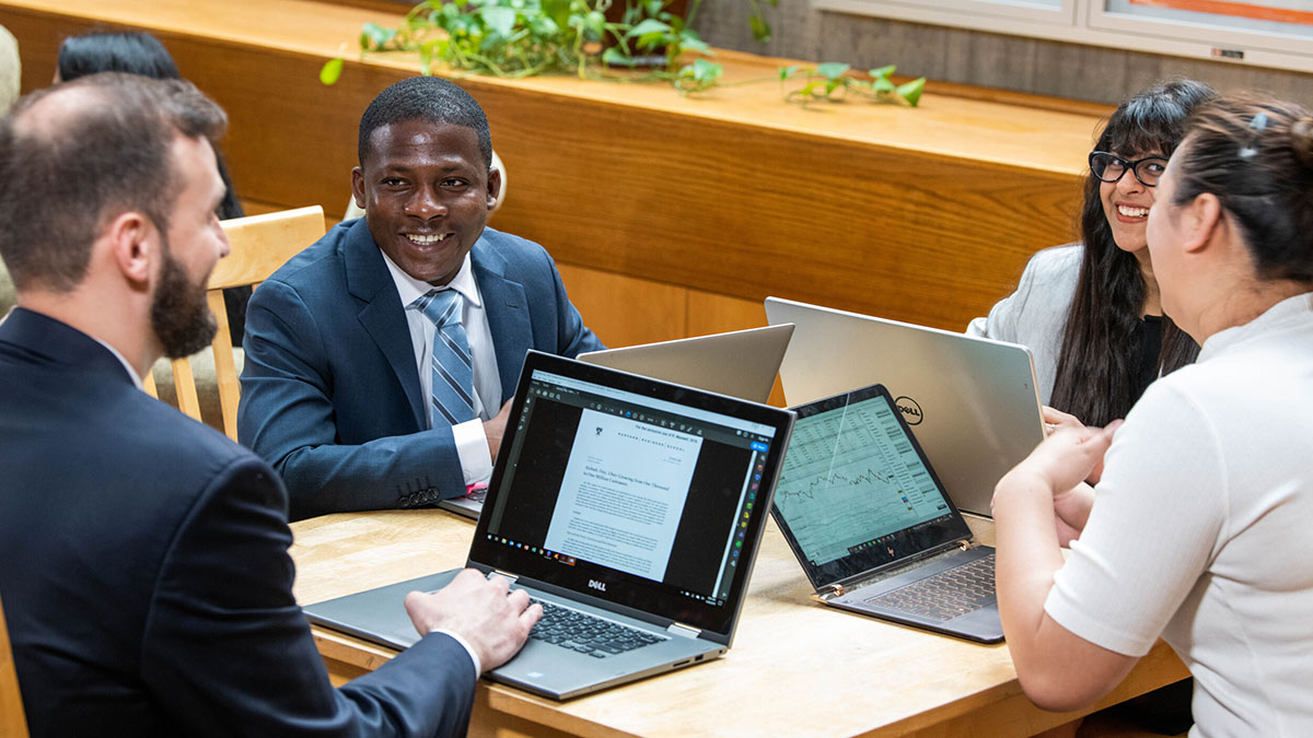 A group of students collaborating at a table with laptops in a casual setting.