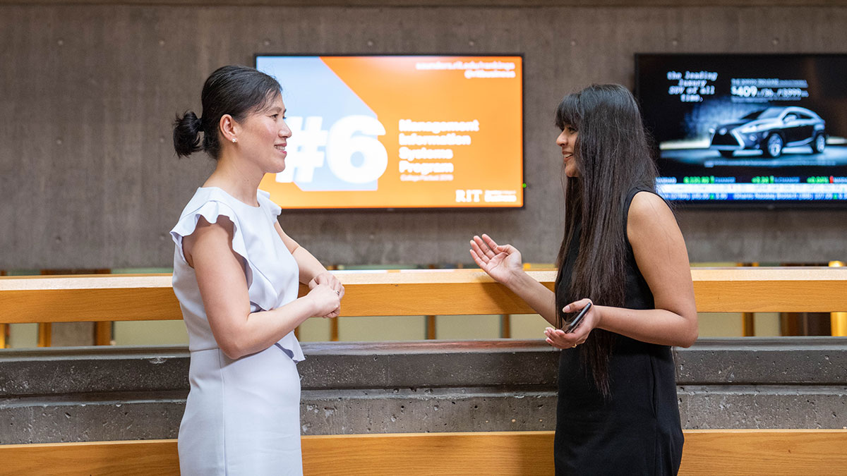 professor and student talking in the atrium of a business school.