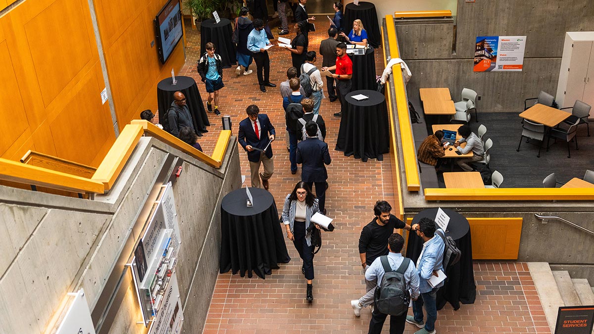A busy university atrium with students and staff interacting around tall round tables.