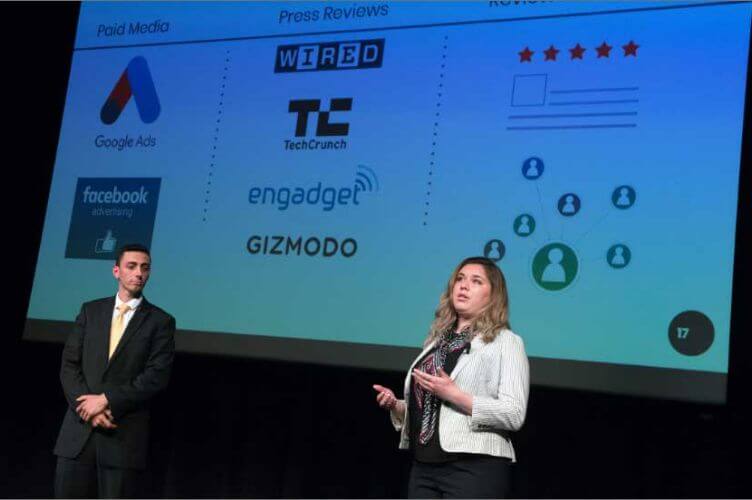 Two R I T students presenting a business plan on stage in front of a screen as part of the BIZ 1+2 course.