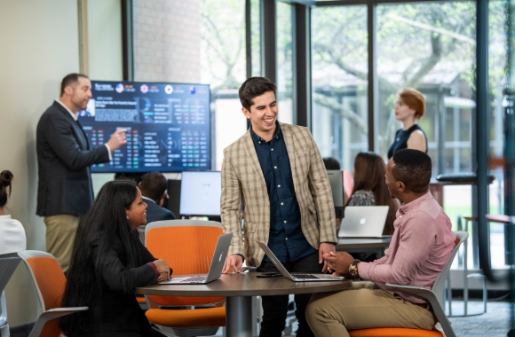 Two people sitting at a desk while one stands behind talking to them