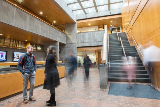 student and professor talk in an atrium as other people walk by, and their motion causes their images to be blurry.